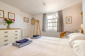 A bedroom with a bed, a dresser, a window with curtains, a radiator, and framed pictures on the wall. - 2 Bed in Polruan (oc-pc023) (Fowey)
