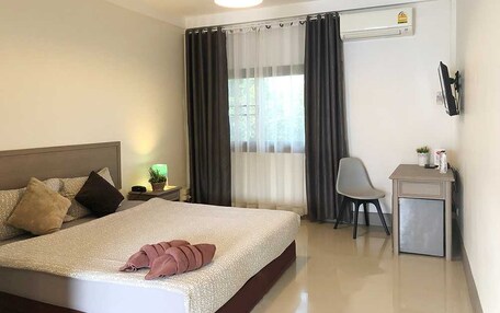 A hotel room with a bed, a desk, a chair, a nightstand, a lamp, and a window with curtains.