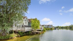 A lakeside property with a dock, a house with a deck, and a row of similar houses in the background.