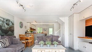 A modern living room with a sofa, a coffee table with plants, a dining area with chairs, and a kitchen with cabinets.