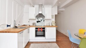 Eine moderne Küche mit weißen Schränken, einer Edelstahl-Dunstabzugshaube und einem eingebauten Backofen. Es gibt eine Holzarbeitsplatte, ein Spülbecken und einen Essbereich mit Tisch und Stühlen.