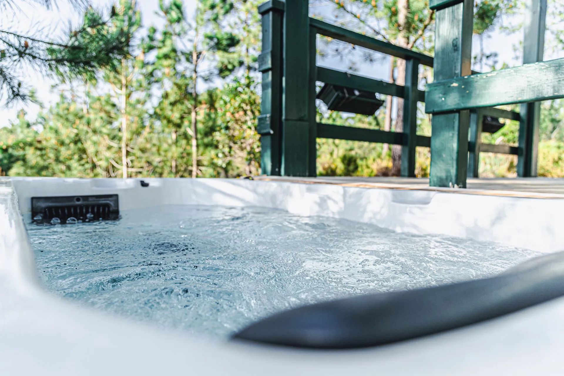 A hot tub with a wooden deck and a view of trees in the background.