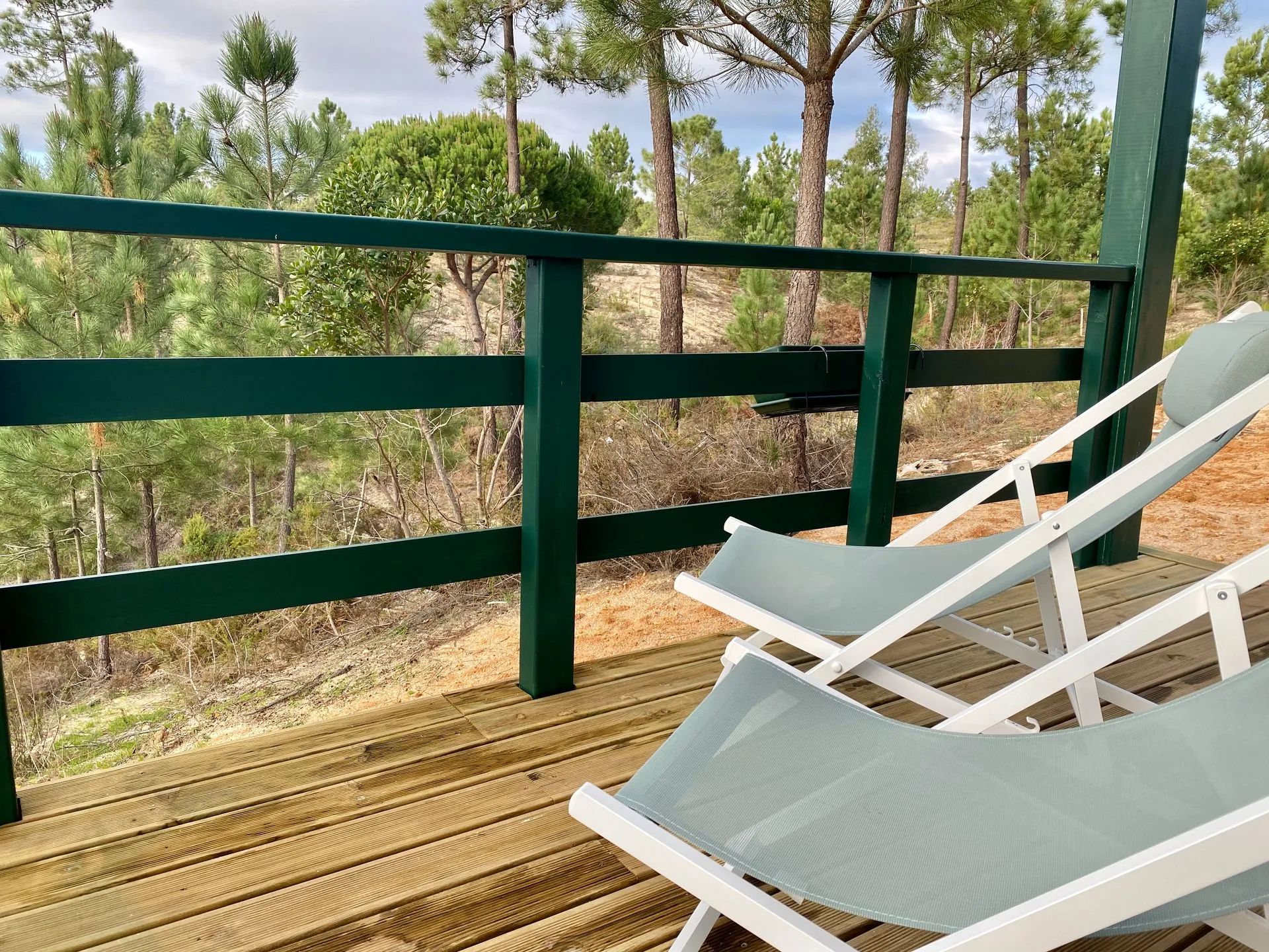 Terraza de madera con barandilla verde y dos sillas reclinables blancas.