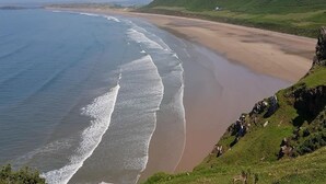 Paesaggio costiero con spiaggia, colline erbose e cielo sereno.