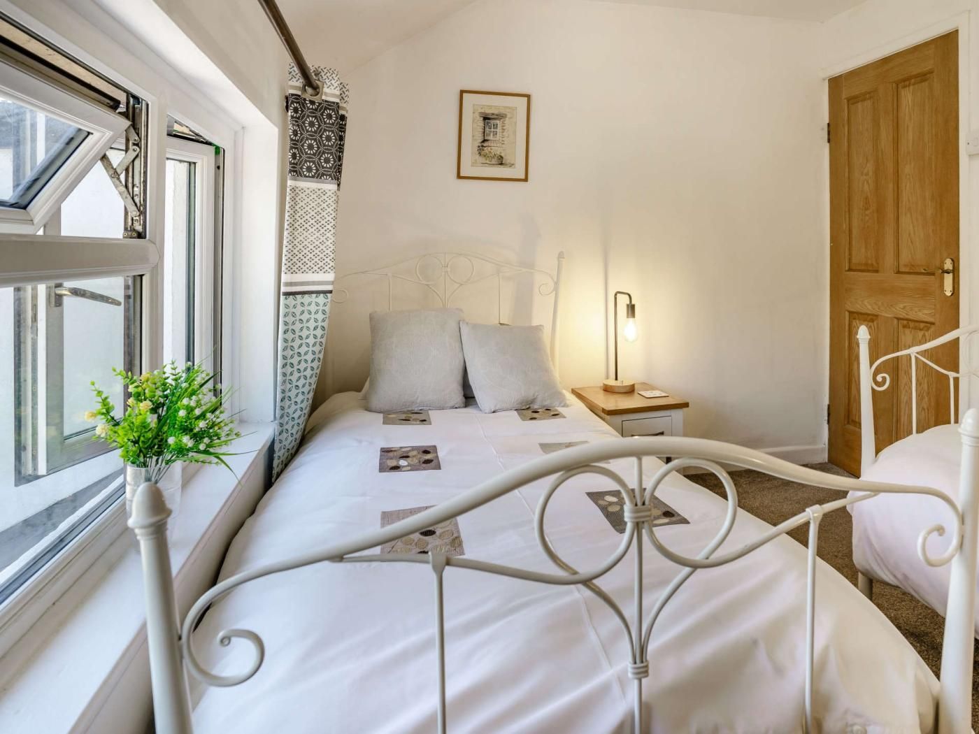 A bedroom with a bed, bedside table, lamp, and a window with curtains.