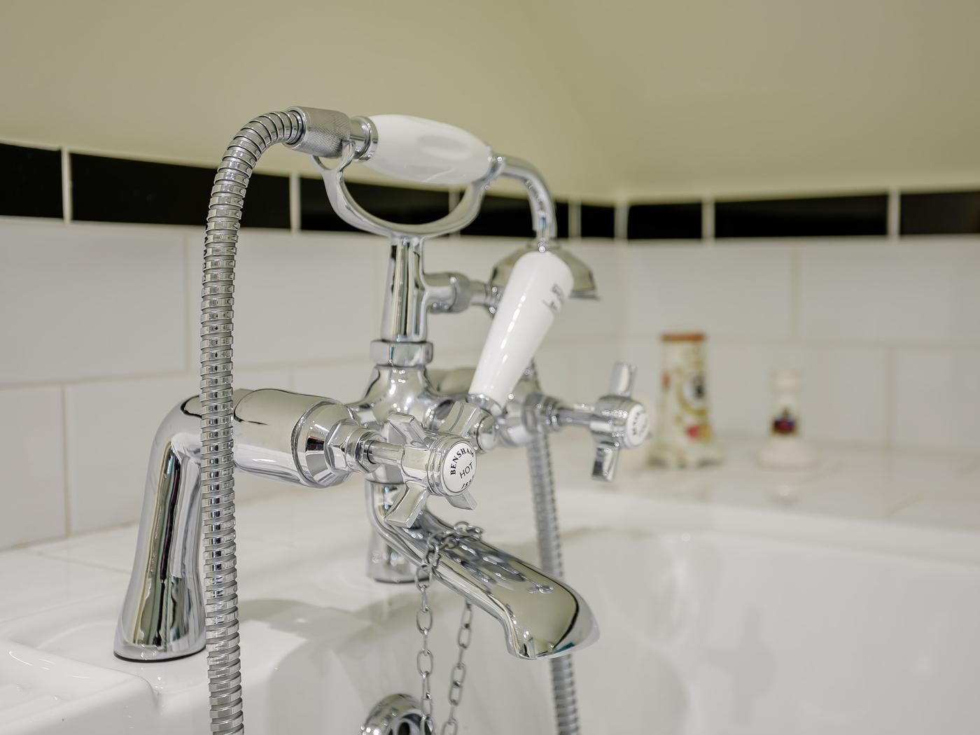 A bathroom with a chrome faucet, a showerhead, and a soap dispenser.