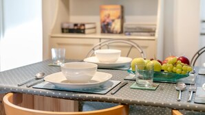 Une table à manger avec des assiettes et des bols blancs, ainsi qu'un verre d'eau. On y trouve des fruits, comme des pommes et des raisins.