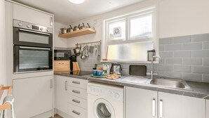Une cuisine compacte équipée d’un four encastré, d’un lave-linge et d’une fenêtre située au-dessus de l’évier.