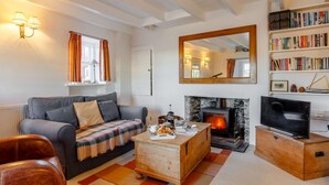 A cozy living room with a fireplace, a sofa, a coffee table, a bookshelf, and a television. - 2 Bed in Polruan (oc-pc033) (Fowey)