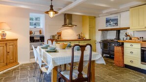 A dining area with a table set for four, a stove, and a window with a view. - 2 Bed in Polruan (oc-pc033) (Fowey)