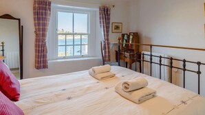 A bedroom with a bed, a window with curtains, a bedside table, and a hanging lamp. - 2 Bed in Polruan (oc-pc033) (Fowey)