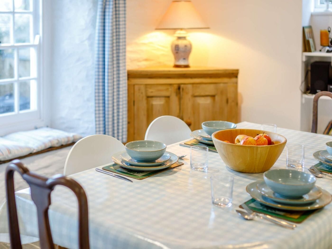 A dining table set with bowls, plates, and glasses, a lamp, and a window with curtains.