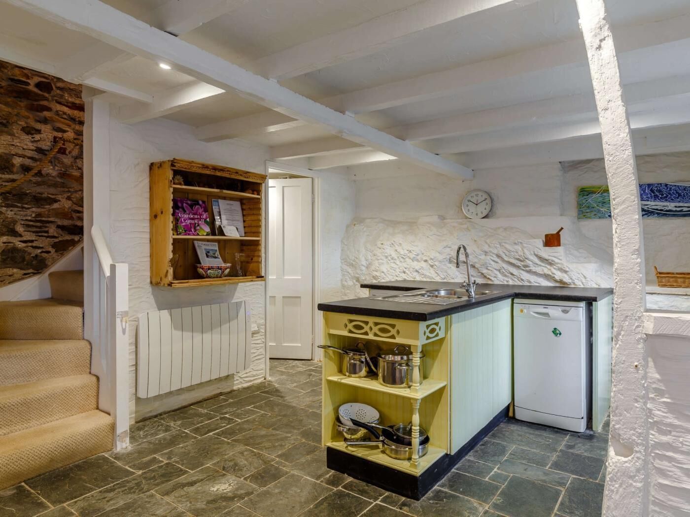 Une cuisine compacte avec un mur en pierre, une étagère en bois avec des livres, un évier et un petit réfrigérateur.