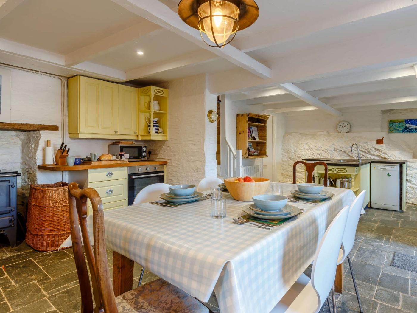 A cozy kitchen with yellow cabinets, a dining table set for four, and a stone wall in the background.