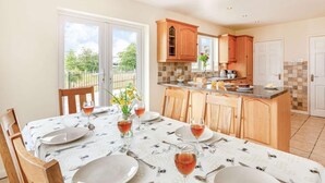 A dining area with a table set for four, a kitchen with wooden cabinets, and a view through the glass door. - 4 Bed in Denbigh (oc-62368) (Denbigh)