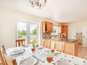 A dining area with a table set for four, a kitchen with wooden cabinets, and a view through the glass door. - 4 Bed in Denbigh (oc-62368) (Denbigh)