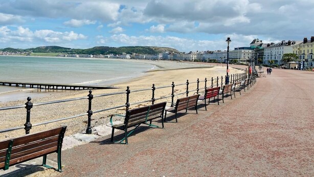 A coastal promenade with benches, a promenade railing, and a view of the sea and distant buildings. - 4 Bed in Denbigh (oc-62368) (Denbigh)