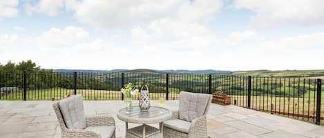 A patio with wicker furniture, a round table, and a view of rolling hills.