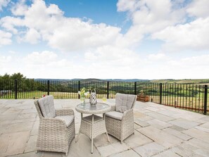 A patio with wicker furniture, a round table, and a view of rolling hills. - 4 Bed in Denbigh (oc-62368) (Denbigh)