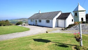 A white building with a garage, a small attached structure, and a gravel driveway. - 4 Bed in Denbigh (oc-62368) (Denbigh)