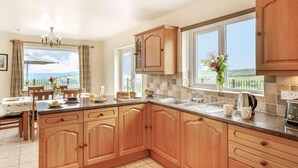 A kitchen with wooden cabinets, a dining area with a table and chairs, and large windows offering a view. - 4 Bed in Denbigh (oc-62368) (Denbigh)