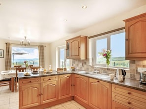 A kitchen with wooden cabinets, a dining area with a table and chairs, and large windows offering a view. - 4 Bed in Denbigh (oc-62368) (Denbigh)