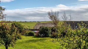 Un paysage rural avec une maison en pierre, des champs verdoyants et un ciel dégagé.