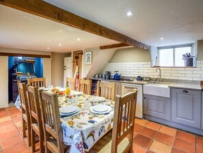 A dining area with a table set for four, wooden chairs, a kitchen with a sink and stove, and a window above the sink. - 4 Bed in Worth Matravers (oc-ic175) (Worth Matravers)