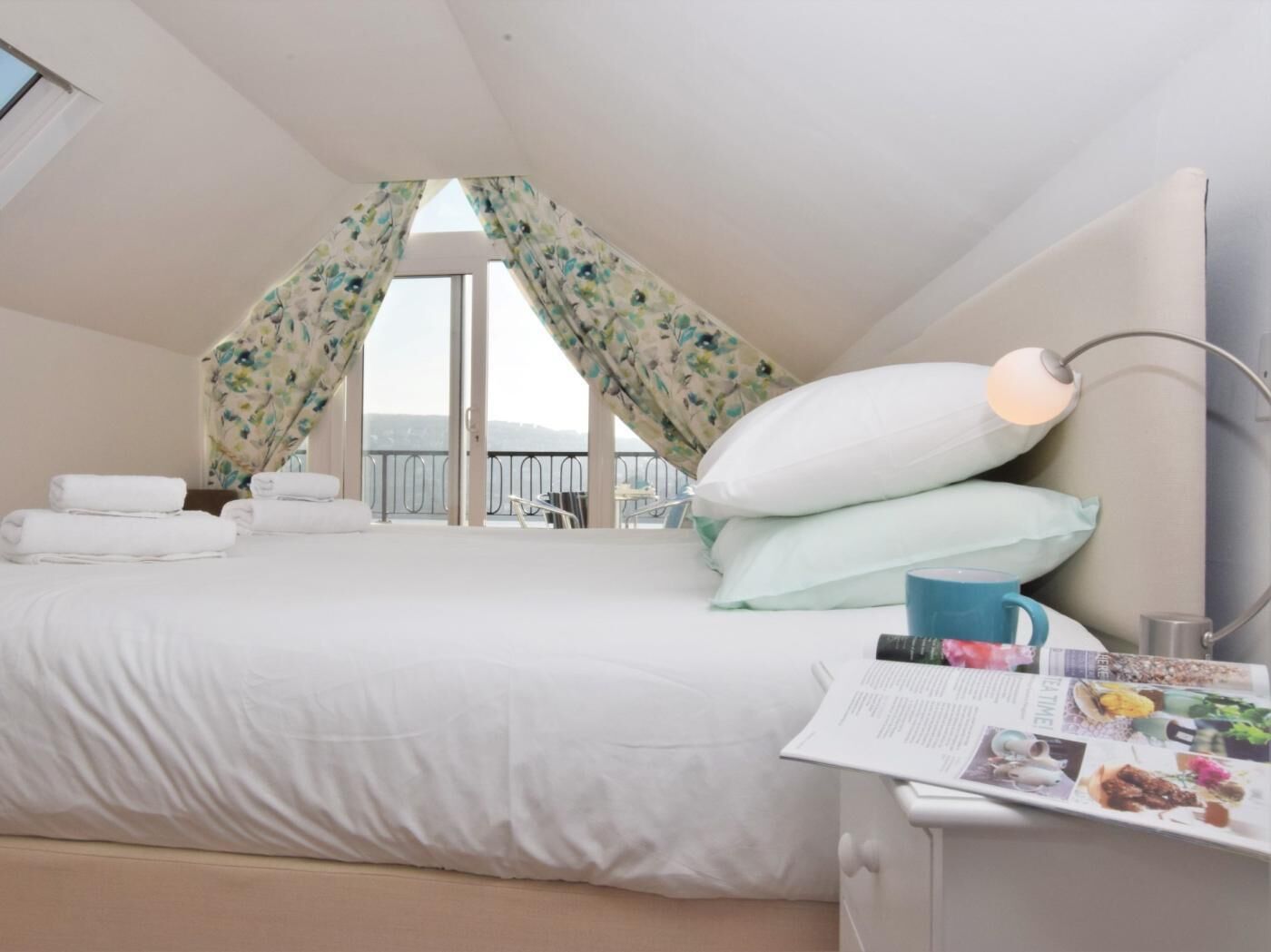 A bedroom with a bed, pillows, a bedside table with a lamp, and a magazine.