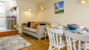 A cozy living room with a sofa, a dining table with chairs, a kitchen area, and a painting on the wall. - 2 Bed in Polruan (oc-pc021) (Fowey)