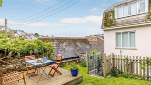 A wooden deck with a table and chairs, a potted plant, and a stone wall. - 2 Bed in Polruan (oc-pc021) (Fowey)