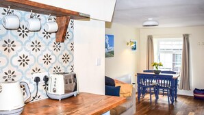A modern kitchen with a wooden countertop, a toaster, and a kettle. There is a dining area with a table and chairs, and a colorful rug on the floor. - 2 Bed in Polruan (oc-pc021) (Fowey)
