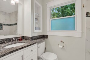 A bathroom with a white vanity, a sink, a toilet, and a window with a view of trees.