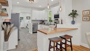 Una cocina moderna con armarios blancos, una isla de madera e iluminación colgante.
