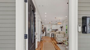 Un pasillo que conduce a una cocina con piso de madera, un comedor con mantel estampado y una puerta con marco negro.