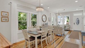 Un comedor espacioso con mesa y sillas de madera, una araña y ventanas amplias con vistas a la vegetación.