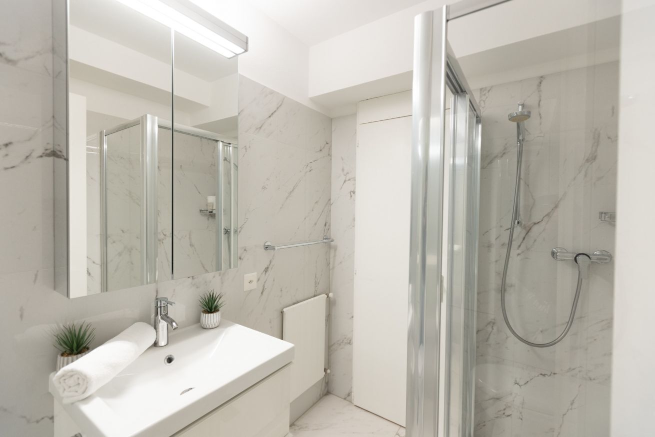 Une salle de bain moderne avec une douche à parois de verre, un lavabo blanc et un mur recouvert de carreaux de marbre.