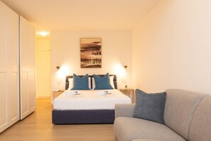Quarto de hotel com uma cama, mesas de cabeceira, um quadro na parede e um sofá.