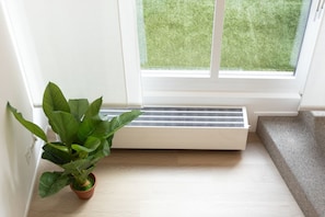 Um canto de um quarto com uma planta em vaso, uma janela com vista para uma área gramada e um radiador branco.