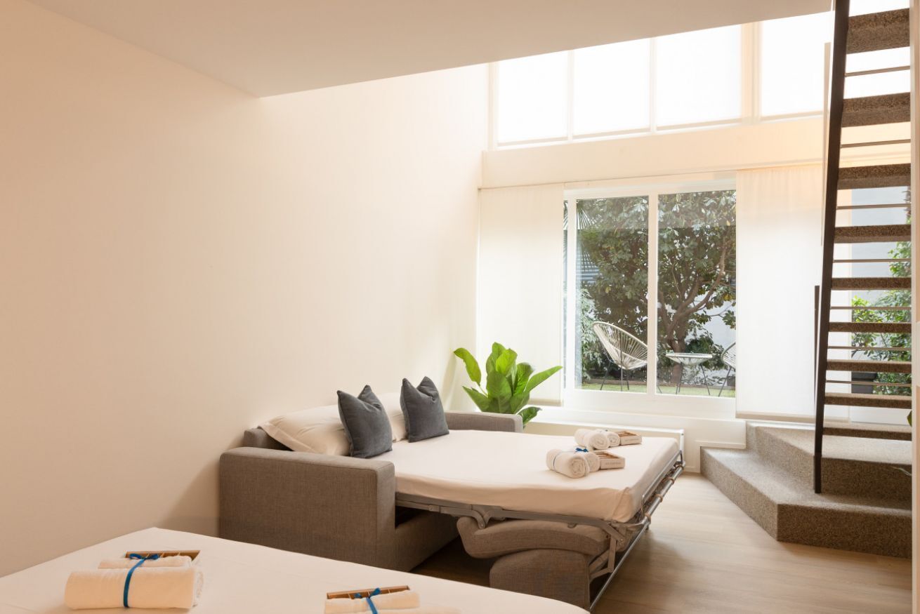 Ein modernes Zimmer mit einem Bett, einer Couch, einem Fenster mit Blick auf Bäume und einer Treppe.