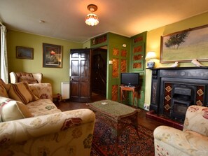 A living room with a sofa, a television, a fireplace, and a door leading to another room. - 3 Bed in Polruan (oc-pc032) (Fowey)