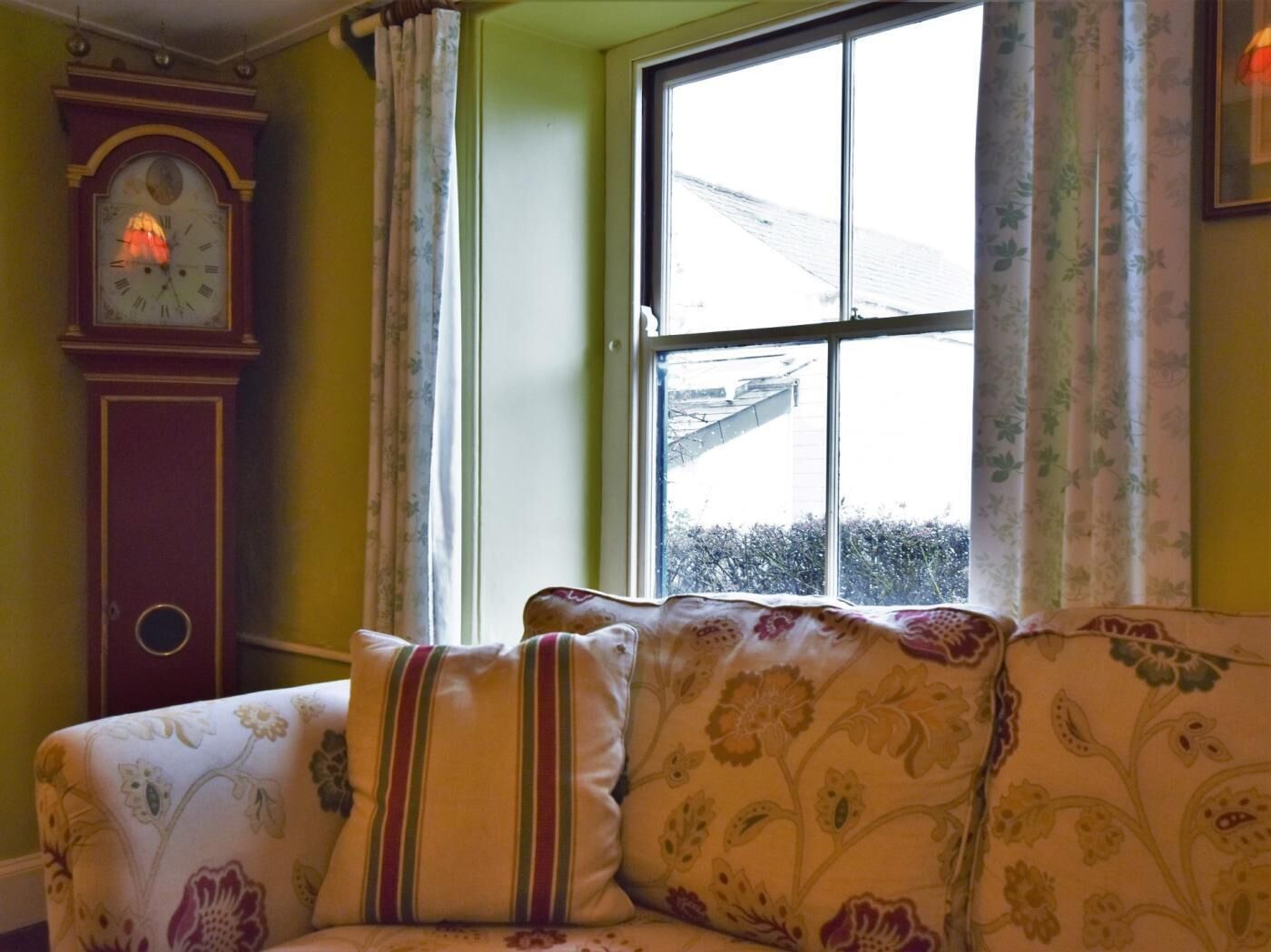 Ein Zimmer mit einer Couch, einer Uhr und einem Fenster mit Vorhängen.