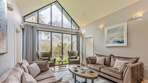 A spacious living room with a high ceiling, large windows, and a view of the outdoors. There are two sofas, a coffee table, and two armchairs. - 3 Bed in Bamburgh (oc-61867) (Bamburgh)
