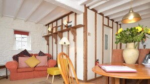 Ein gemütliches Wohnzimmer mit einem roten Sofa, einem Holzstuhl, einem Streifen Teppich und einem Holztisch mit einer Blumenvase.