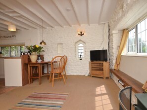 Ein gemütlicher Raum mit Steinwand, einem Holztisch mit Stühlen, einem Fernseher auf einem Holzschrank und einem Fenster mit Vorhängen.