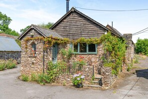 Une petite maison en pierre avec un toit en pente, un petit porche et une fenêtre ornée d’un volet vert.