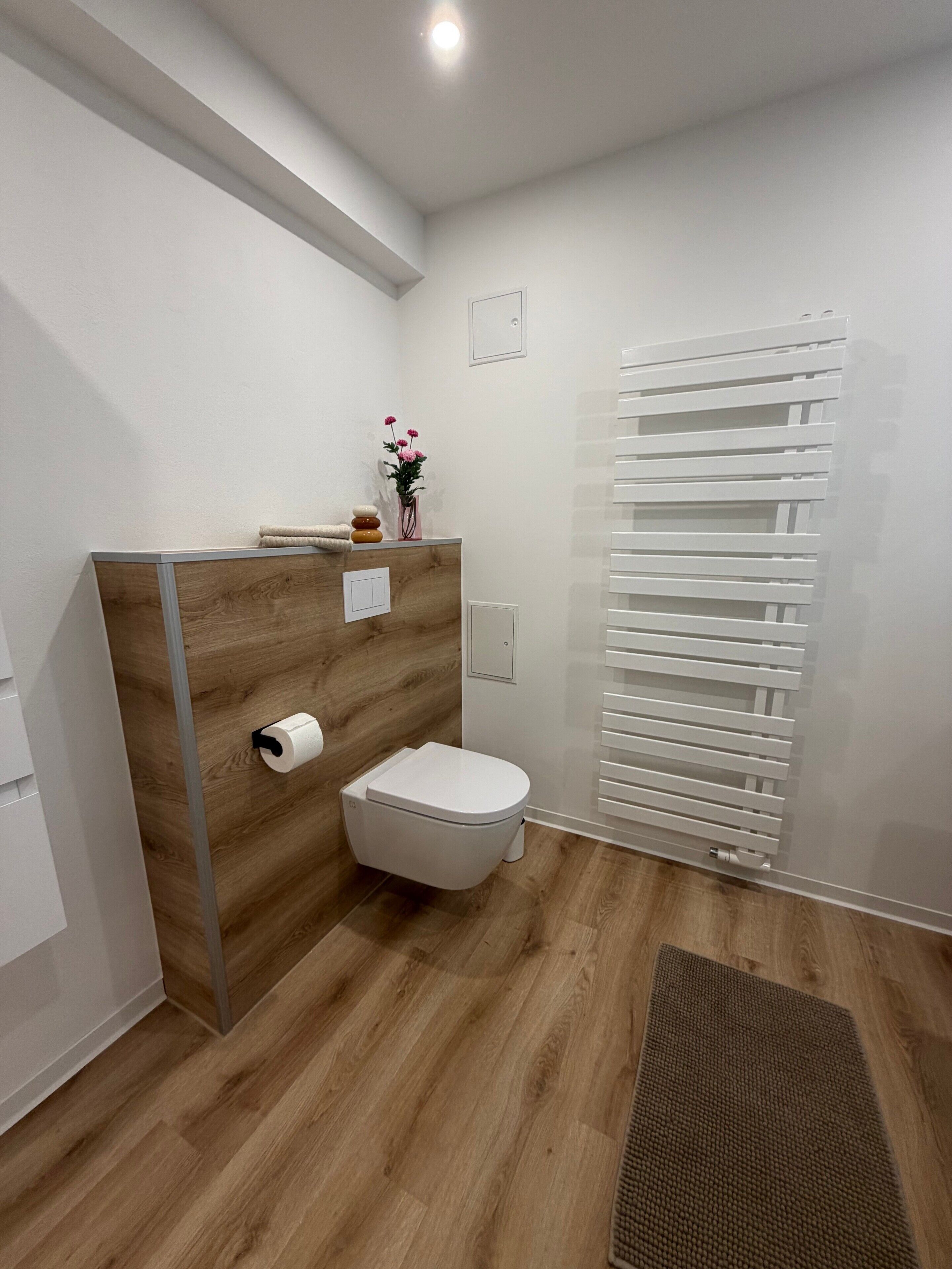 Ein modernes Badezimmer mit einem Holz-Waschtisch, Toilette und einem weißen Handtuchwärmer.
