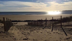 Una playa con una valla de madera, terreno arenoso y un atardecer sobre el agua.
