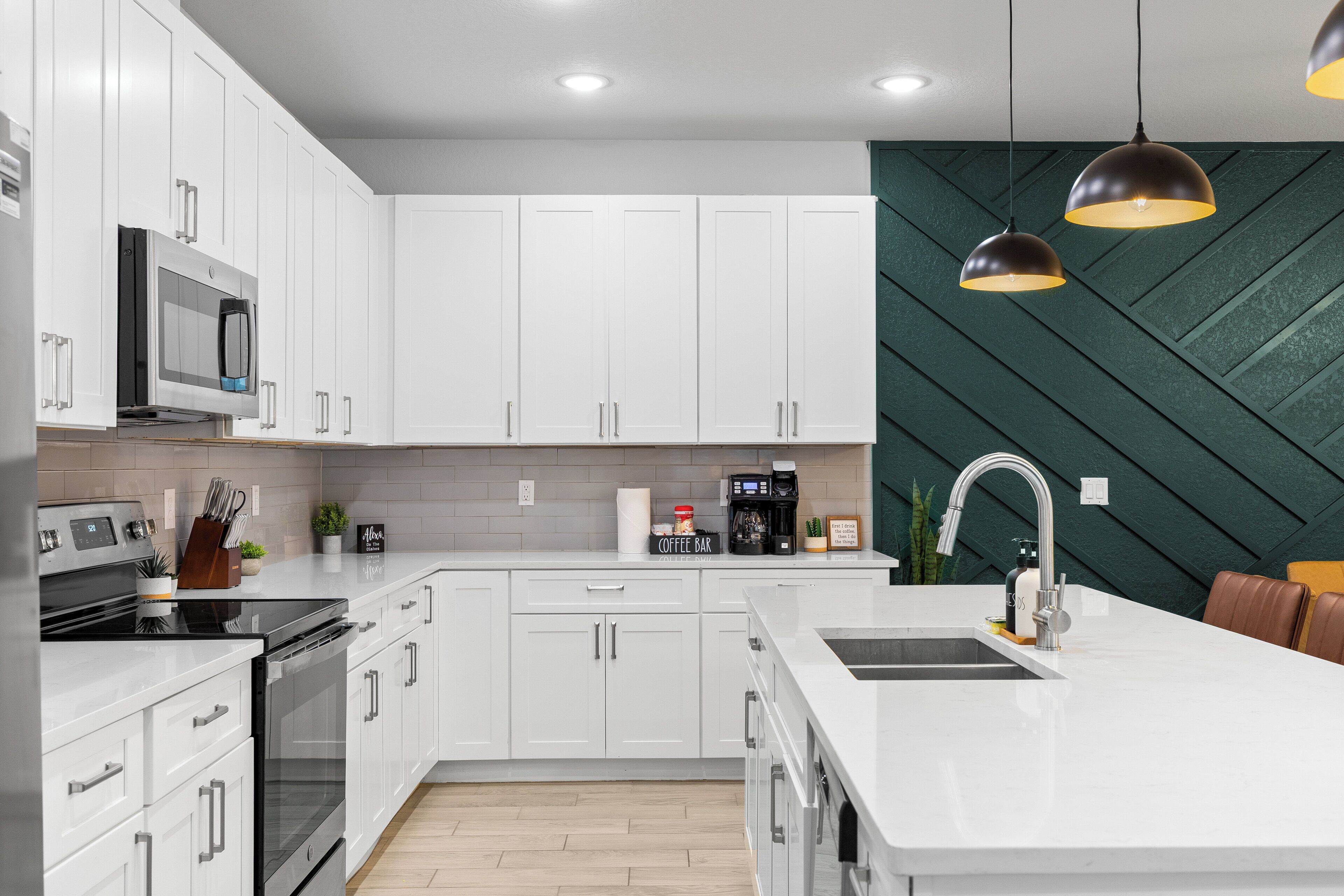 A modern kitchen with white cabinets, a stainless steel range, a coffee station, and a unique green wall pattern.