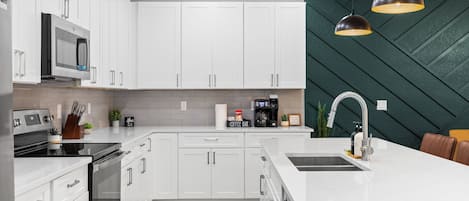 A modern kitchen with white cabinets, a stainless steel range, a coffee station, and a unique green wall pattern.
